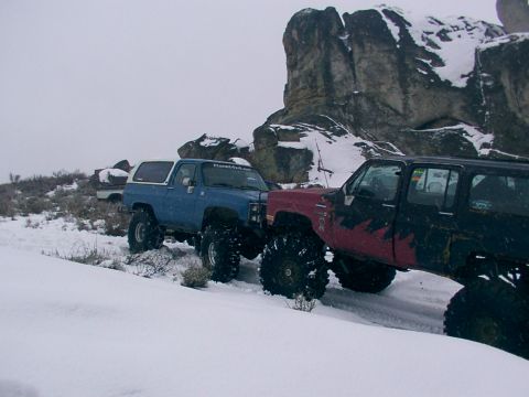 2003 Ford Ranger - Two modified off-road vehicles navigate a snowy terrain with large rock formations in the background.