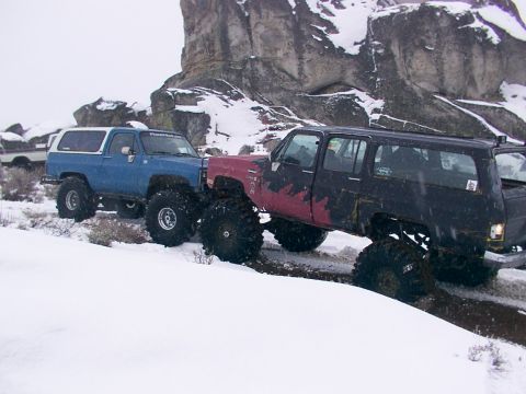 2003 Ford Ranger - Two heavily modified SUVs navigate a snowy trail with large tires and lifted suspensions.