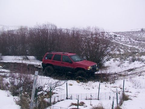 2003 Ford Ranger - A red Jeep Grand Cherokee is stuck in a muddy, snow-covered ditch, with trees and hills in the background.