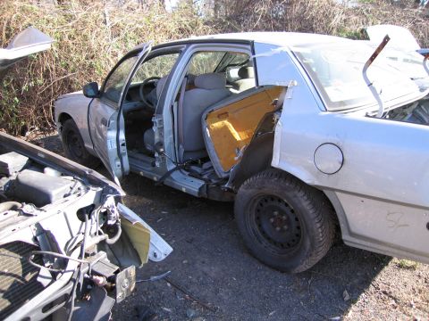 1991 Ford LTD Crown Victoria - A damaged sedan sits in a yard with its doors open, revealing the interior. Another vehicle's front end is partially visible.