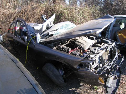 1991 Ford LTD Crown Victoria - A severely damaged 1991 Ford Crown Victoria LTD sits in a junkyard, its front end crushed and hood open.