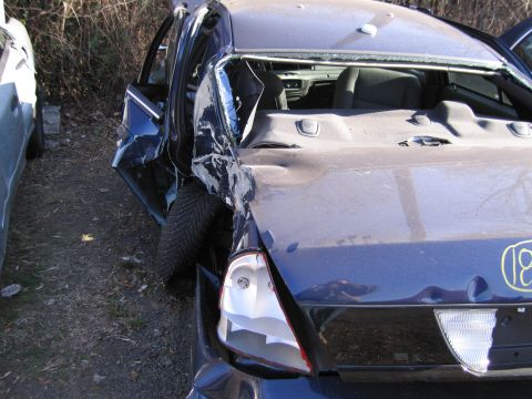 1991 Ford LTD Crown Victoria - This dark blue sedan sustained severe rear-end damage, with a broken taillight and visible tire, and a yellow '18' marking on its trunk.