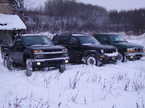 2000 Chevrolet Tahoe - Three trucks and SUVs are stuck in the snow near a wooden structure.