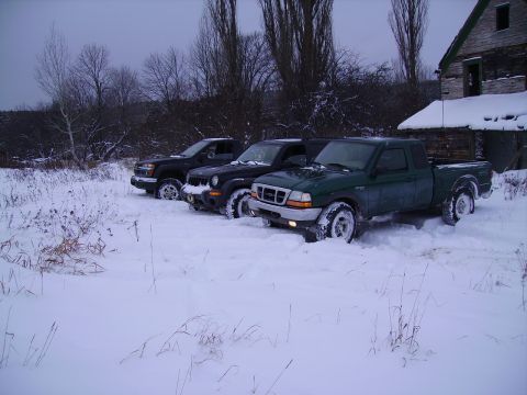 2000 Chevrolet Tahoe - Three trucks are stuck in deep snow next to a weathered wooden structure on a cloudy day.