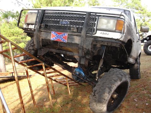 1989 Ford Bronco - Mud-covered 1989 Ford Bronco with aftermarket bull bar and off-road tires on a ramp.