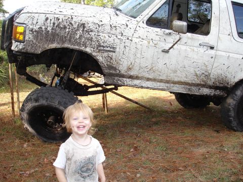 1989 Ford Bronco - A muddy white SUV is shown from the front-right, lifted with large tires, with a child in the foreground.