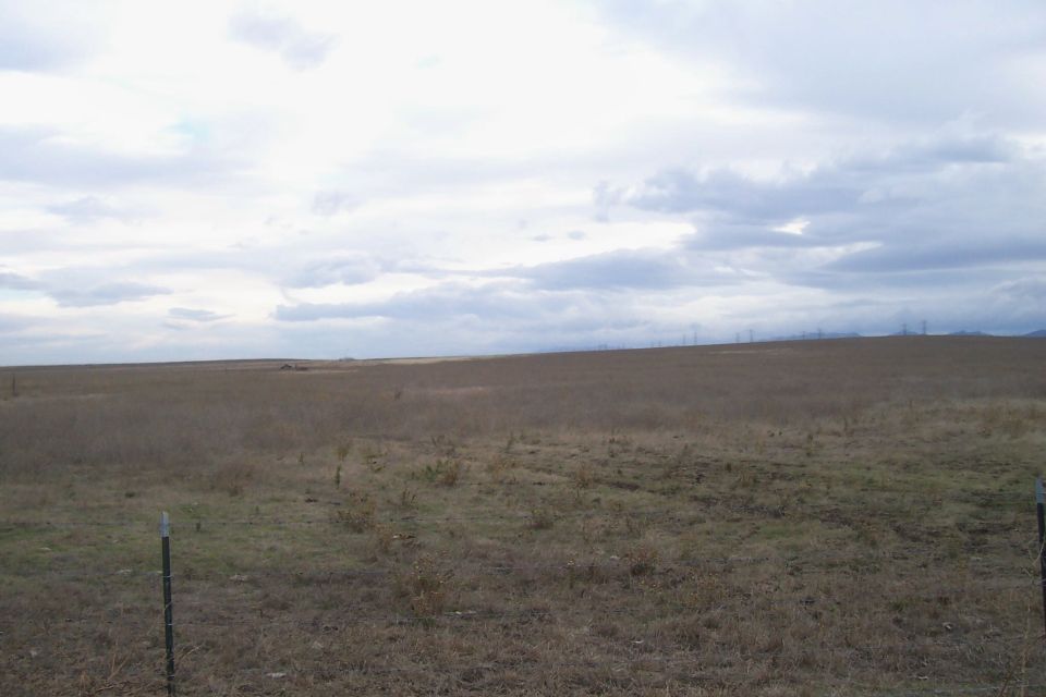 wide shot of a dry, grassy field with fence posts and a cloudy sky