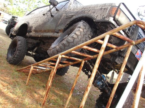 1989 Ford Bronco - This heavily modified off-road vehicle is covered in mud and positioned on a rusty metal ramp.