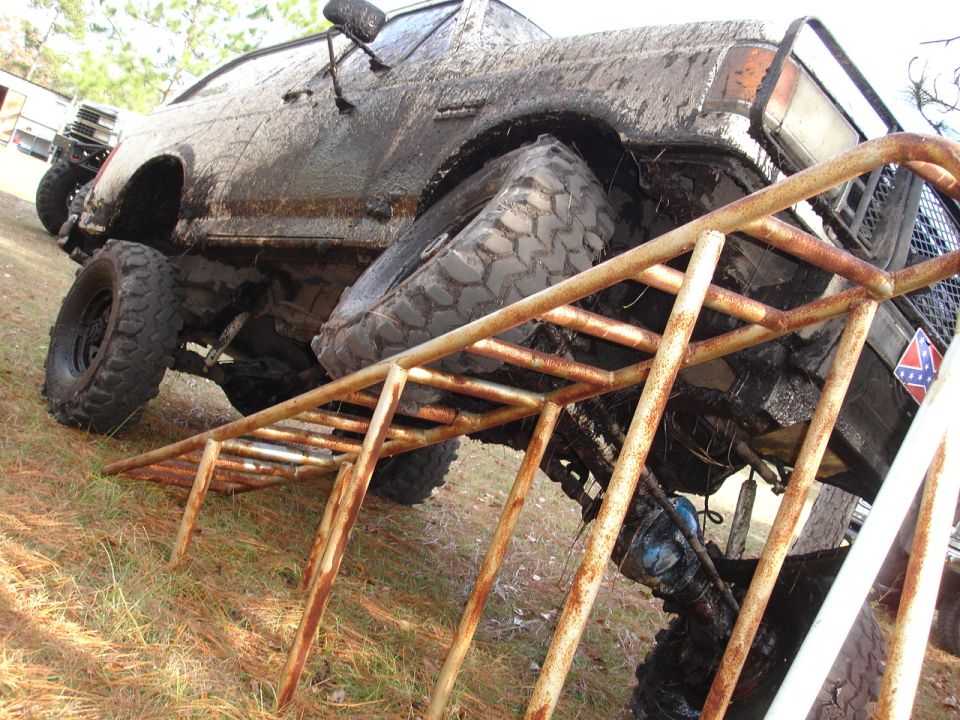 Muddy off-road truck on a rusty metal ramp. Another vehicle is visible behind it