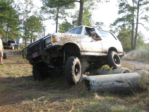 1989 Ford Bronco - A heavily modified SUV navigates an obstacle course, kicking up dirt and water.
