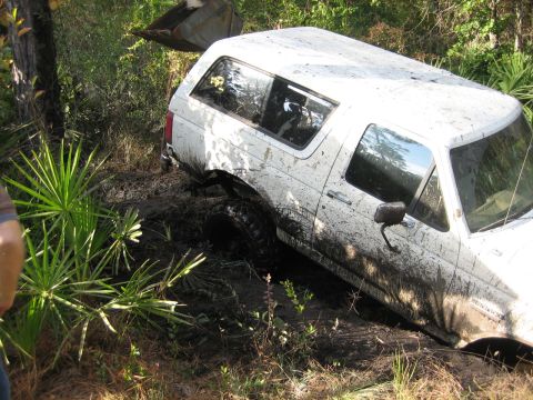 1989 Ford Bronco - A white Ford Bronco is stuck in the mud, with a front loader visible in the background.