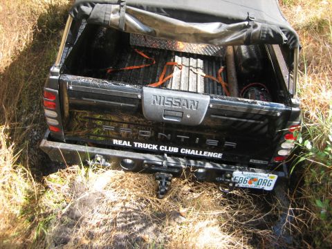 1989 Ford Bronco - A black Nissan Frontier pickup truck is partially submerged in grass and mud, with its tailgate visible.