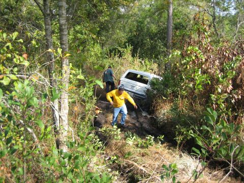 1989 Ford Bronco - Two men are trying to free a white pickup truck that is stuck in the mud.