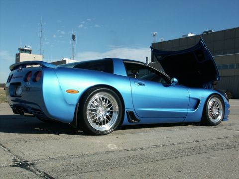 2001 Mercury Grand Marquis - Blue Chevrolet Corvette C5 Z06 parked on concrete with hood open, clear sky overhead.