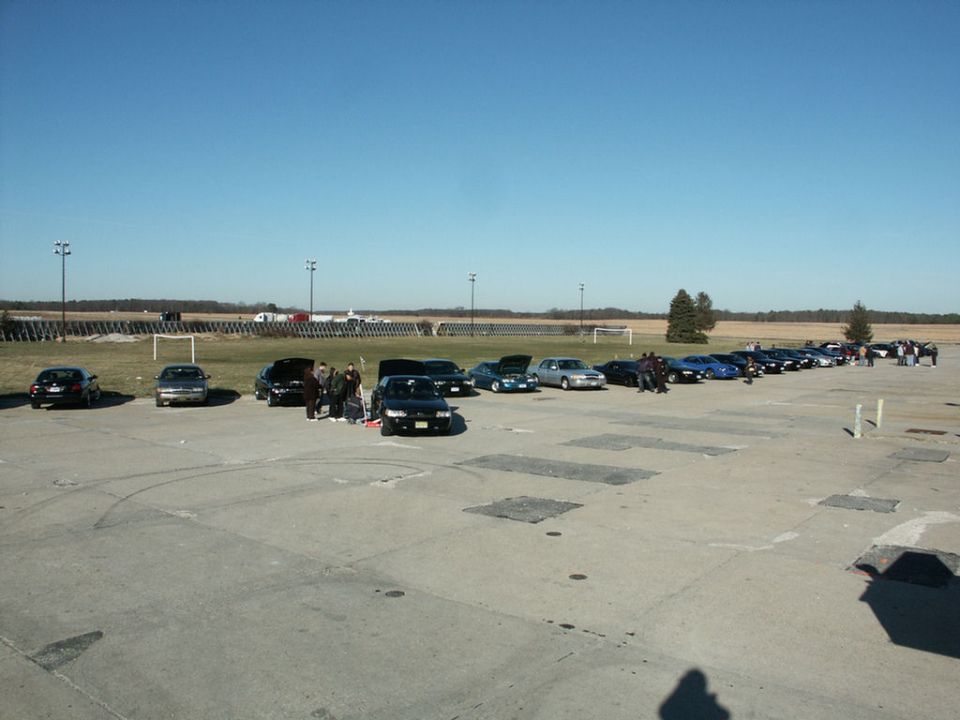 Several black sedans and a silver sedan parked on asphalt under a clear blue sky