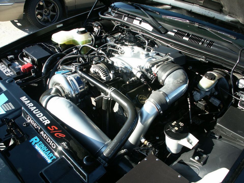 Engine bay with supercharger, intake piping, and "Marauder S/c Tiger Audio Reinhart Automotive" text on a black cover