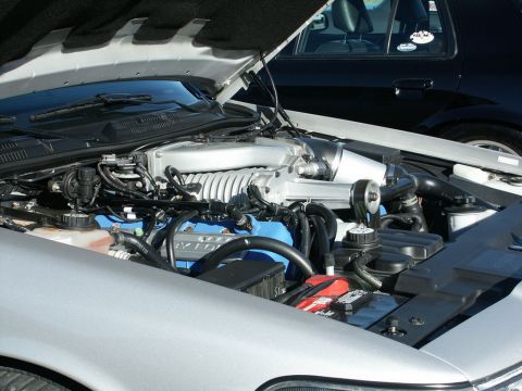 2001 Mercury Grand Marquis - Engine bay of a silver car a supercharger and blue valve covers, with another vehicle visible in the background.