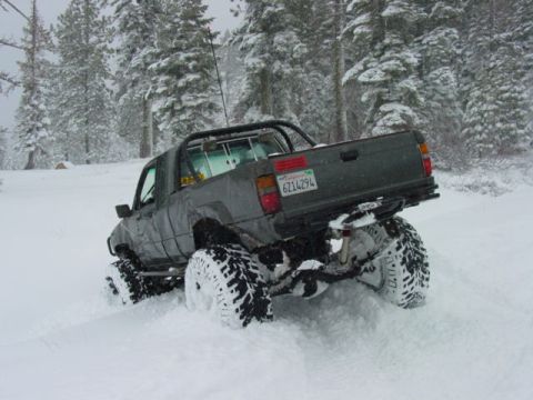 1986 Ford Bronco - Modified pickup truck navigates snowy terrain with large off-road tires.