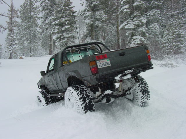 Pickup truck with large tires driving in deep snow, trees in background