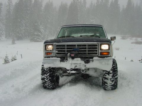 1986 Ford Bronco - A dark blue Ford Bronco navigates a snow-covered terrain during a snowfall.