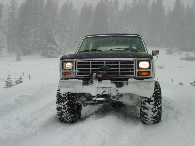 Dark blue Ford Bronco with large tires covered in snow, facing forward in a snowy landscape