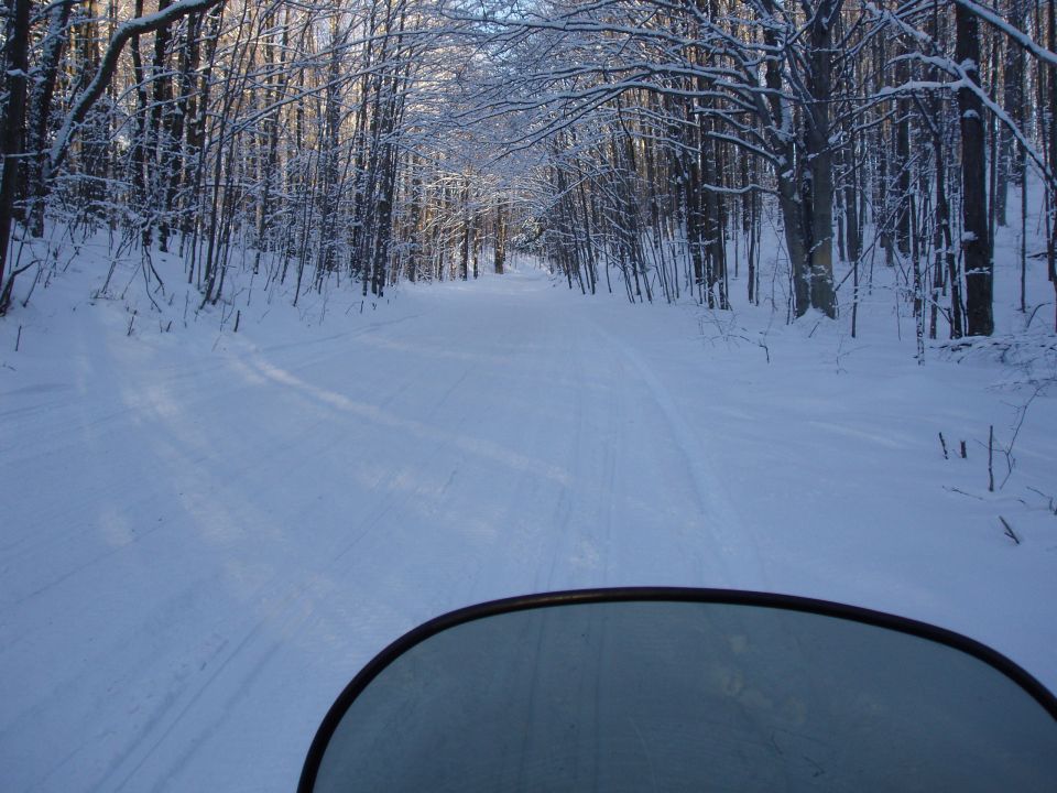 Snowmobile windshield view of a snowy forest road