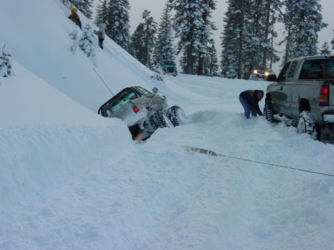 1986 Ford Bronco - Two trucks are stuck in a snowy landscape, with people attempting to free one of them.