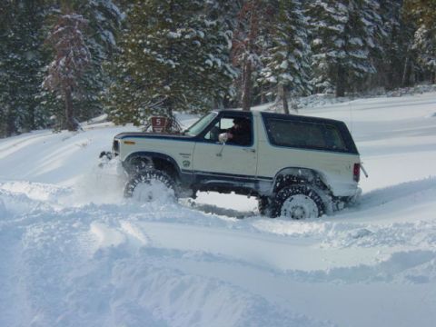 1986 Ford Bronco - A Ford Bronco navigates a snowy terrain with trees visible in the background.