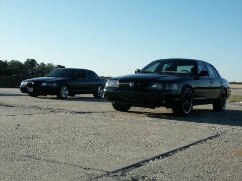 2001 Mercury Grand Marquis - Two black 2001 Mercury Grand Marquis sedans are parked side-by-side on a paved surface under a clear blue sky.