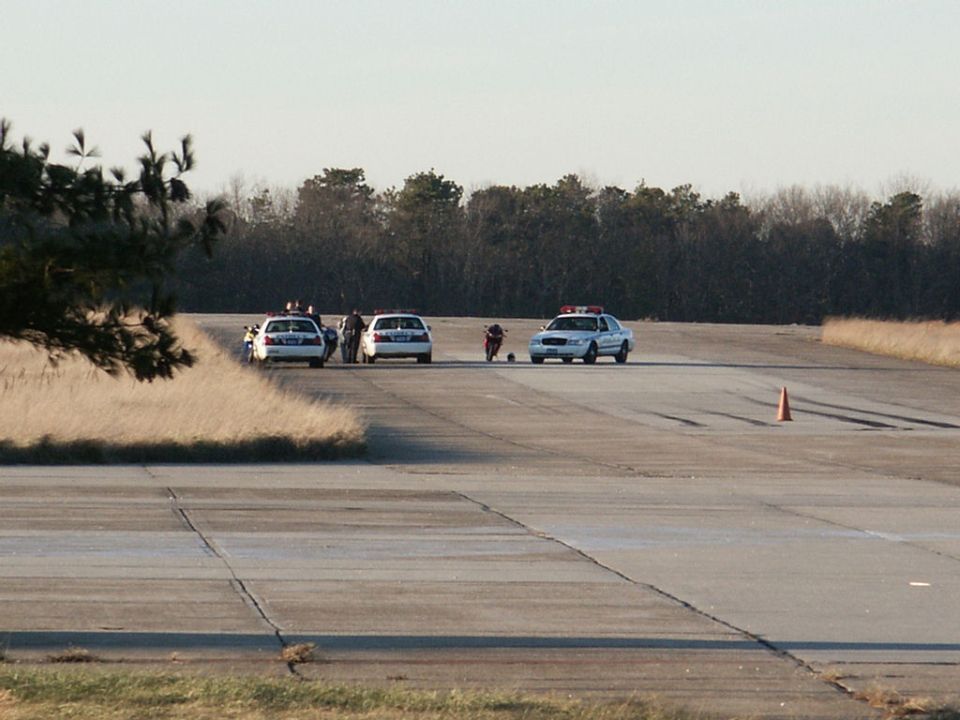 police cars and a motorcycle on a runway with a traffic cone