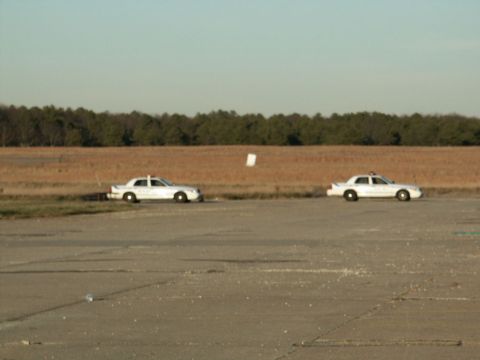 2001 Mercury Grand Marquis - Two white police cars are visible from the side on a clear day with a wooded area in the distance.