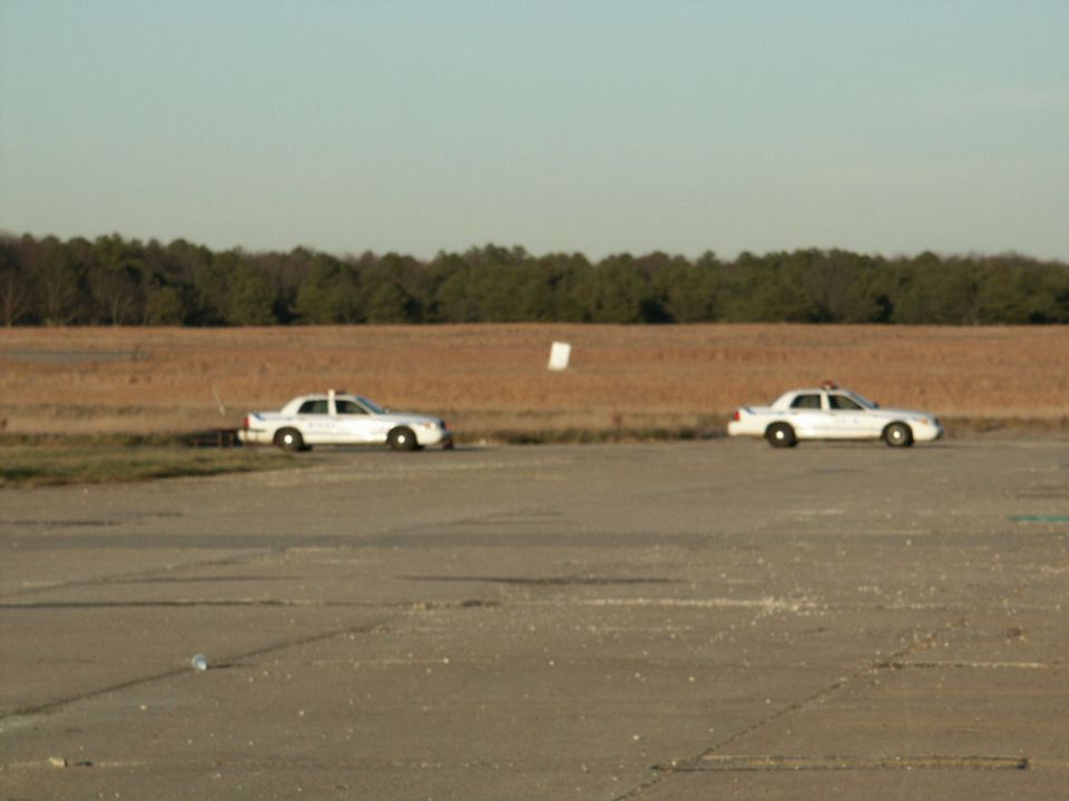 Two white police cars parked on asphalt with a wooded area in the background