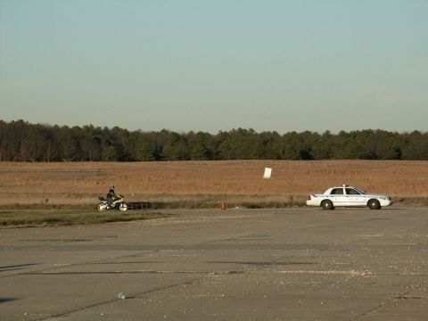 2001 Mercury Grand Marquis - A white police car and a motorcycle are parked on a tarmac with a wooded area in the background.