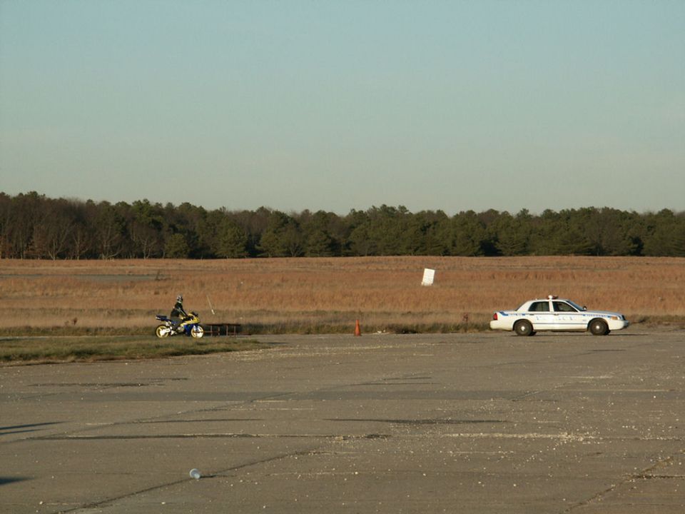 Side view of a white police car and a motorcycle on a tarmac
