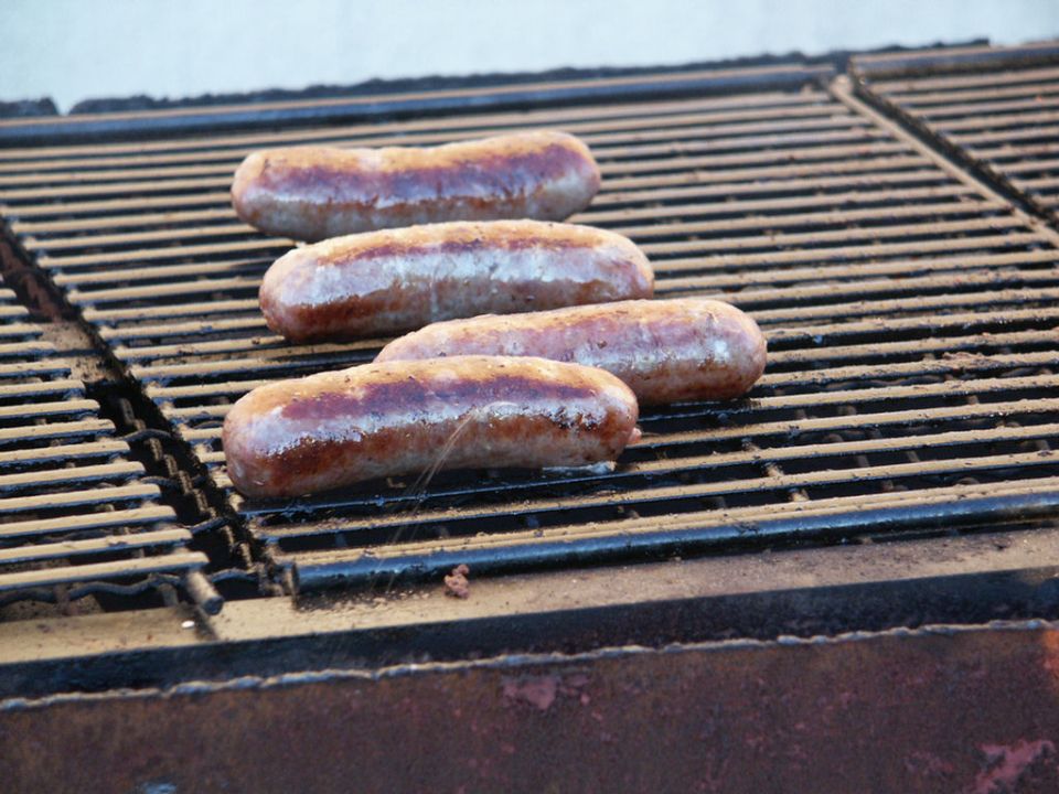 Four sausages cooking on a metal grill grate
