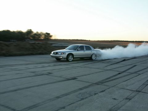 2001 Mercury Grand Marquis - A silver 2001 Mercury Grand Marquis drifts on a paved surface, creating a large cloud of smoke.