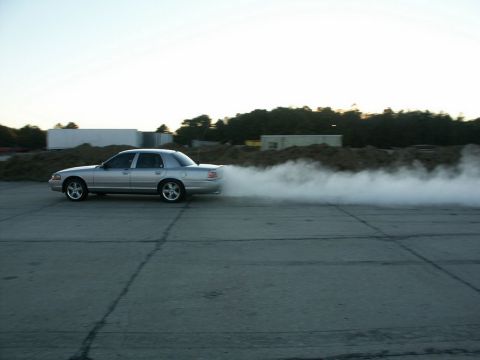 2001 Mercury Grand Marquis - A silver 2001 Mercury Grand Marquis is captured mid-burnout, kicking up a large cloud of smoke.