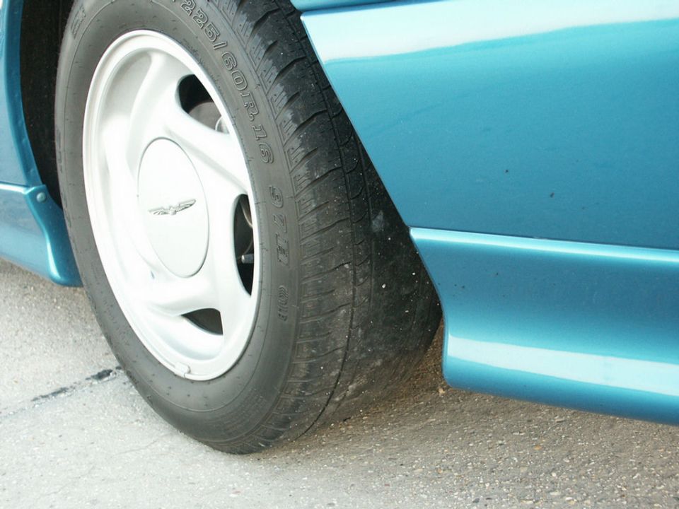 Close-up of a teal car's front wheel and fender skirt. Tire size 225/60R16 is visible