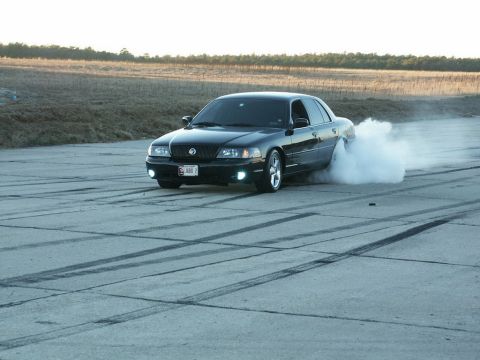 2001 Mercury Grand Marquis - A black sedan performs a burnout on a paved surface, leaving tire marks and smoke.