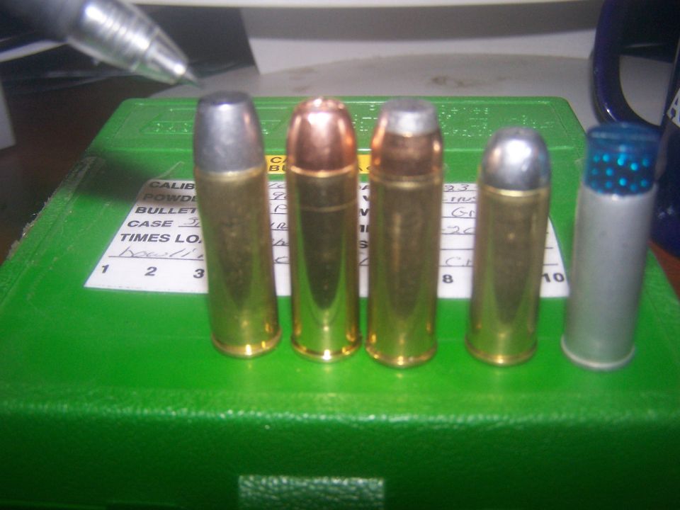Five cartridges lined up on a green ammo box with a pen in the background