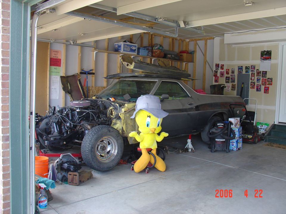 Black 1973 Ford Ranchero under restoration in garage with exposed engine and large Tweety Bird plush beside it