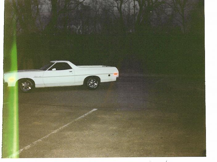 White Ford Ranchero in side profile parked on an empty lot at dusk, with a green film streak on the left.