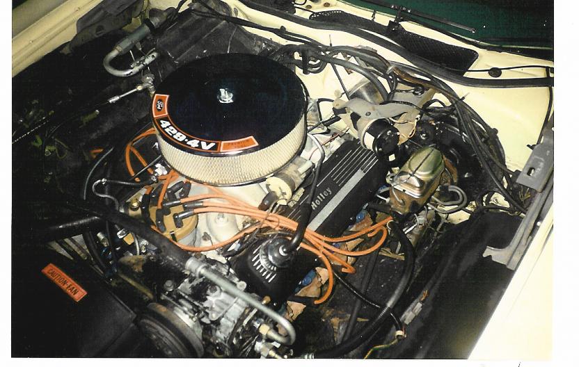 Engine bay with Ford 428 4V air cleaner, Holley valve cover, and orange plug wires in a pale yellow car