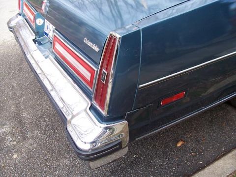 1999 Ford Crown Victoria - Rear view of a blue Oldsmobile showing its chrome bumper, taillight assembly, and side marker.