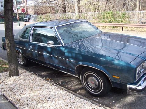 1999 Ford Crown Victoria - This dark teal coupe, seen from a 3/4 front angle, is likely a 1977 Oldsmobile Cutlass Supreme, not the 1999 Ford Crown Victoria listed in…