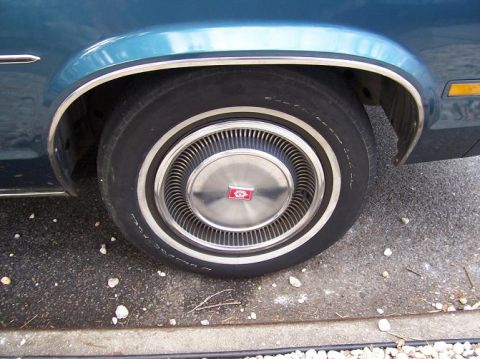 1999 Ford Crown Victoria - Car wheel detail showing a chrome hubcap with a red emblem and a whitewall tire.