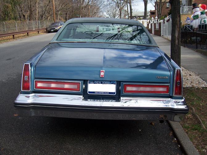 Blue sedan rear view, New York license plate, chrome bumper, parked on street