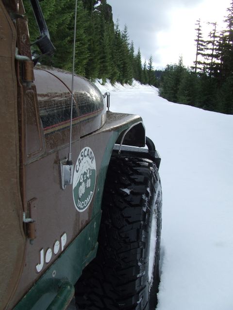 1976 Ford F-150 - A Jeep navigates a snowy mountain road, its tires gripping the icy surface.