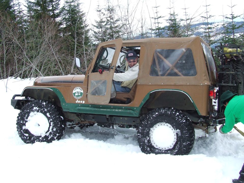 Brown Jeep Wrangler with tan soft top stuck in snow, driver visible