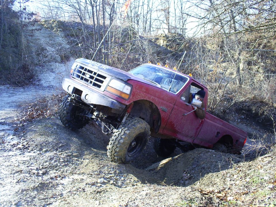 Red Ford F-series truck with large tires climbing a dirt hill